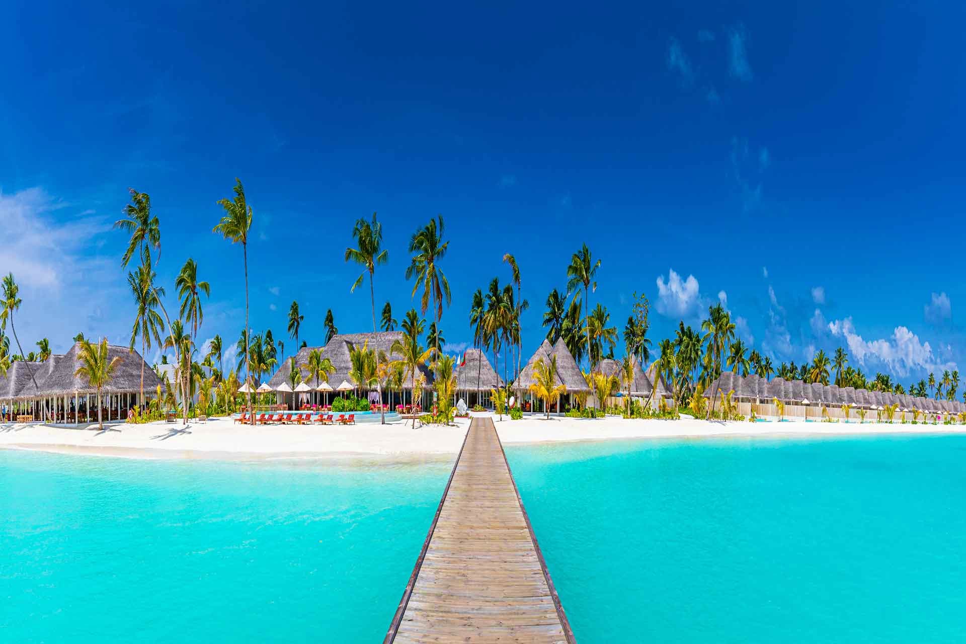Philippines Visa Wooden boardwalk leading to tropical beach resort with thatched-roof bungalows, palm trees, and turquoise water in Maldives